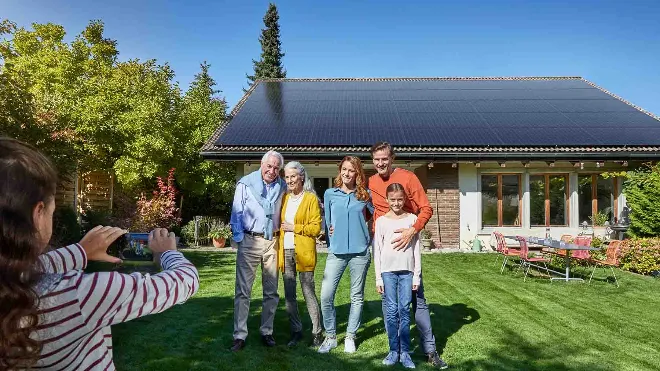 Die Familie eines zufriedenen Kunden von EKZ steht vor ihrem Einfamilienhauses. Auf dem Dach erzeugt eine Photovoltaikanlage sauberen Strom, mit dem das Elektroauto geladen wird.