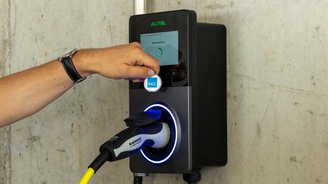 Eine Person hält den EKZ Zugangschip an den RFID-Leser der Ladestation und schaltet damit den Ladevorgang frei.