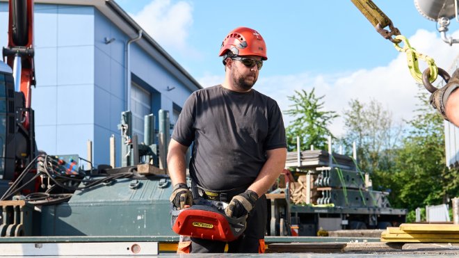 Ein Mitarbeiter des Transportunternehmens hebt einen Trafo mittels Lastkran auf den Anhänger.