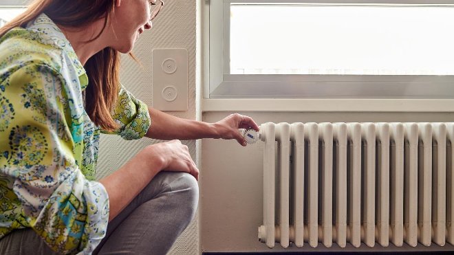 Frau dreht am Heizungsthermostat